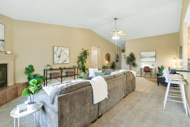 living room with ceiling fan, a fireplace, vaulted ceiling, and light carpet