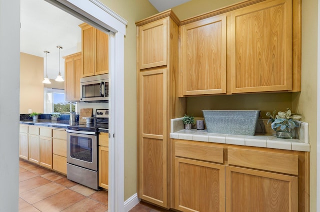 kitchen featuring pendant lighting, stainless steel appliances, light tile patterned flooring, light brown cabinetry, and tile countertops