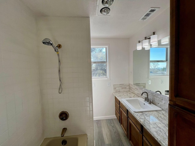 bathroom with tiled shower / bath combo, vanity, hardwood / wood-style flooring, and a textured ceiling