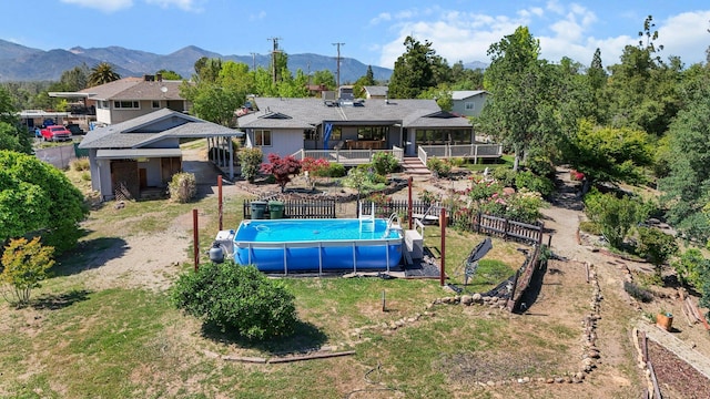 back of property with a lawn, fence, an outdoor pool, and a deck with mountain view