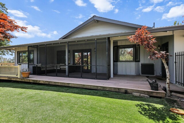 rear view of house featuring a lawn, a sunroom, and a deck
