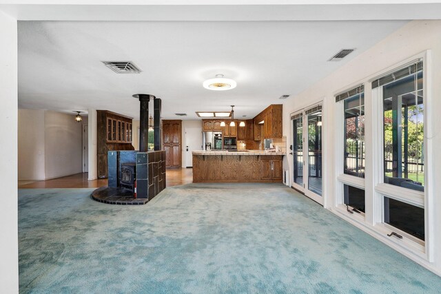interior space featuring a peninsula, visible vents, a wood stove, and light colored carpet