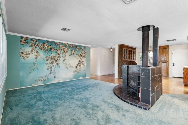 unfurnished living room with a wood stove, baseboards, ornamental molding, and visible vents
