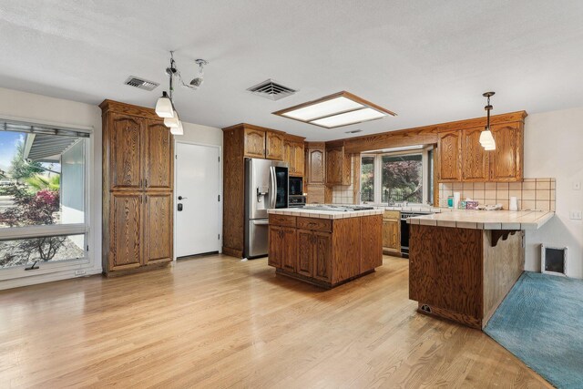 kitchen with a peninsula, stainless steel fridge, visible vents, and tile countertops