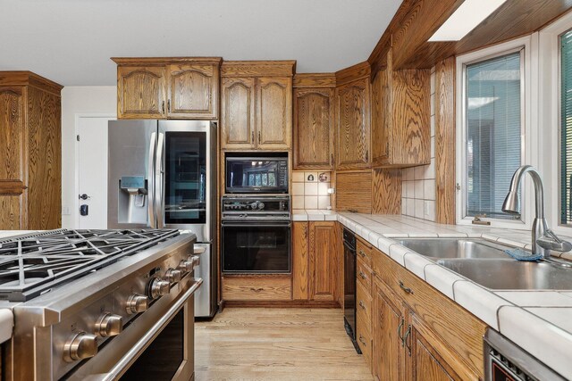 kitchen featuring tile counters, brown cabinets, a sink, light wood-style floors, and black appliances