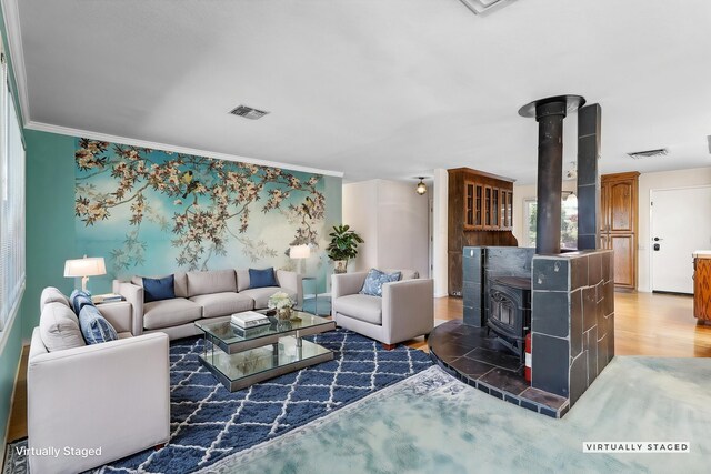 living area featuring ornamental molding, a wood stove, wood finished floors, and visible vents