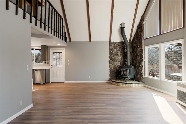 unfurnished living room featuring hardwood / wood-style floors, a wood stove, and a high ceiling