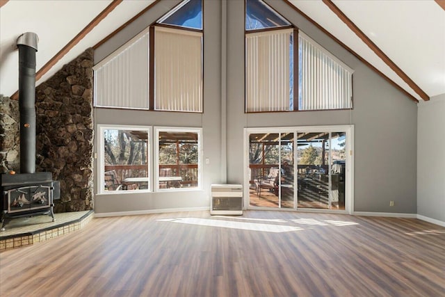 unfurnished living room featuring hardwood / wood-style flooring, plenty of natural light, a wood stove, and high vaulted ceiling