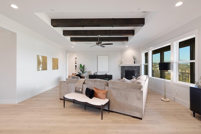 living room featuring beam ceiling, light wood-type flooring, ornamental molding, ceiling fan, and a premium fireplace