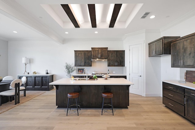 kitchen featuring a kitchen island with sink, beam ceiling, a kitchen breakfast bar, and decorative backsplash