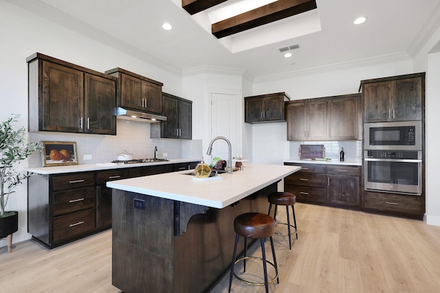 kitchen featuring built in microwave, gas stovetop, stainless steel oven, a kitchen breakfast bar, and a kitchen island with sink