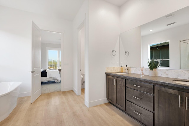 bathroom with vanity, a bath, wood-type flooring, decorative backsplash, and toilet