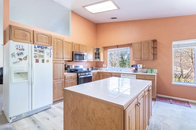 kitchen with appliances with stainless steel finishes, high vaulted ceiling, tile counters, a kitchen island, and light brown cabinetry