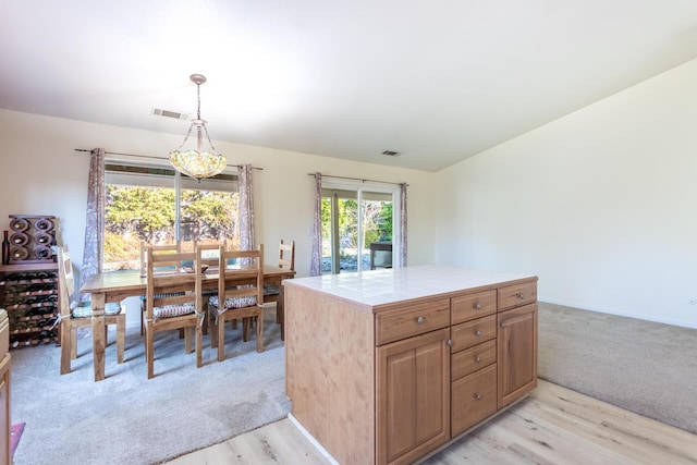 kitchen featuring tile counters, a center island, hanging light fixtures, and light hardwood / wood-style flooring