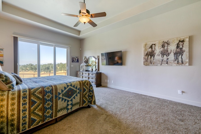 carpeted bedroom with access to exterior, a tray ceiling, and ceiling fan