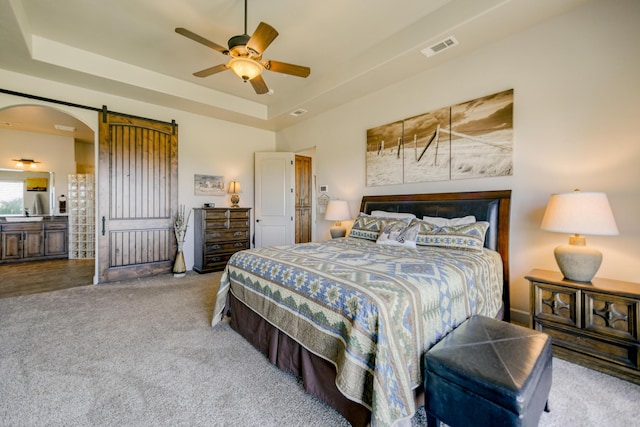 carpeted bedroom with a raised ceiling, ceiling fan, and a barn door