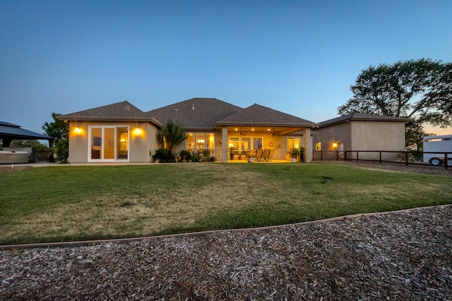 back house at dusk featuring a lawn, a patio, and ceiling fan