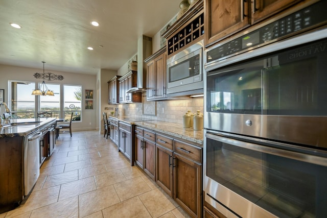 kitchen featuring sink, light stone counters, tasteful backsplash, appliances with stainless steel finishes, and pendant lighting