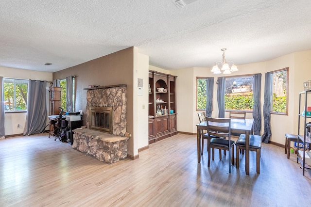 dining space with a stone fireplace, an inviting chandelier, a textured ceiling, and light wood-type flooring