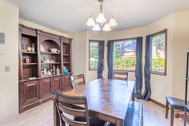 dining room with light hardwood / wood-style floors, a textured ceiling, and a notable chandelier