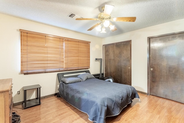 bedroom featuring multiple closets, ceiling fan, light hardwood / wood-style floors, and a textured ceiling