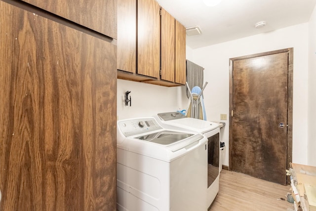 laundry area featuring cabinets, washing machine and clothes dryer, and light hardwood / wood-style floors