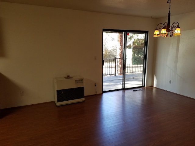 empty room with heating unit, visible vents, dark wood-style flooring, and a notable chandelier