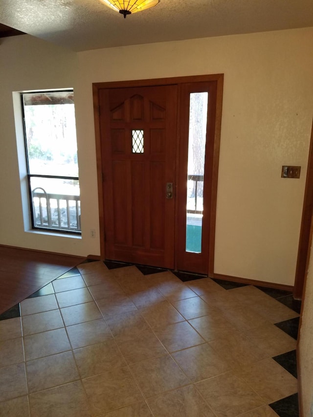 foyer entrance featuring a textured ceiling, baseboards, and light tile patterned floors