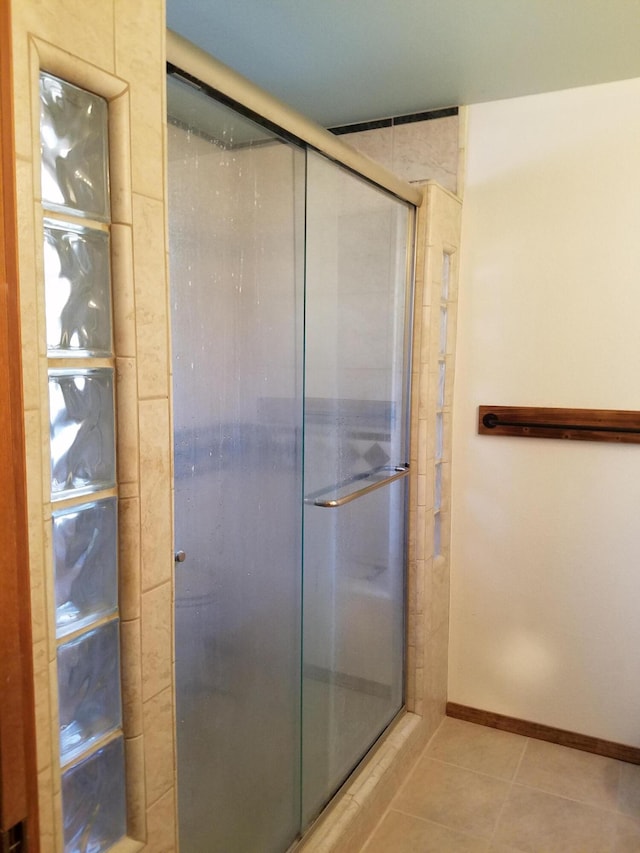 full bathroom with a stall shower, tile patterned flooring, and baseboards