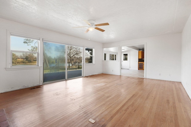 unfurnished living room featuring ceiling fan, a healthy amount of sunlight, light hardwood / wood-style flooring, and a textured ceiling