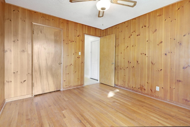 spare room featuring hardwood / wood-style flooring, ceiling fan, a textured ceiling, and wood walls