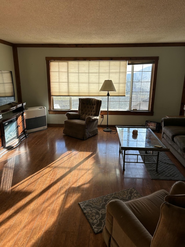 living room with heating unit, hardwood / wood-style floors, crown molding, and a textured ceiling