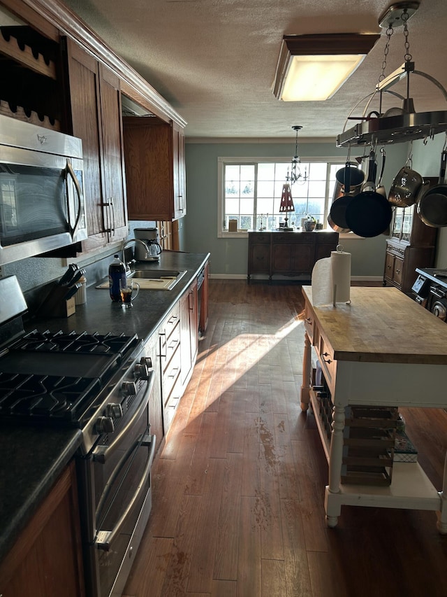 kitchen with appliances with stainless steel finishes, butcher block countertops, sink, dark hardwood / wood-style flooring, and a textured ceiling