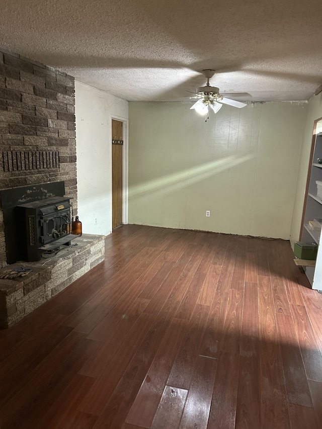 unfurnished living room featuring ceiling fan, hardwood / wood-style flooring, a textured ceiling, and a wood stove