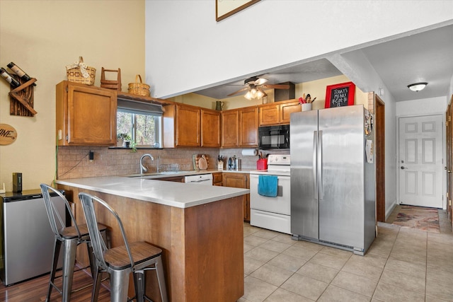 kitchen with sink, a breakfast bar area, kitchen peninsula, white appliances, and backsplash