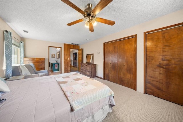 bedroom with light carpet, ceiling fan, a textured ceiling, and multiple closets