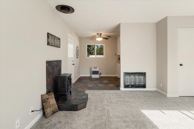 carpeted living room featuring ceiling fan, a textured ceiling, heating unit, and a wood stove