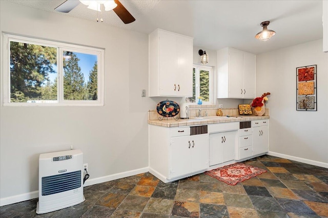 kitchen featuring tile countertops, heating unit, white cabinetry, sink, and ceiling fan