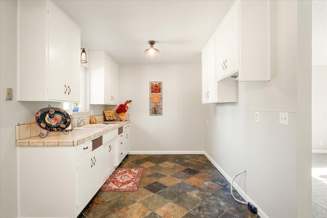 kitchen featuring sink, tile counters, and white cabinets