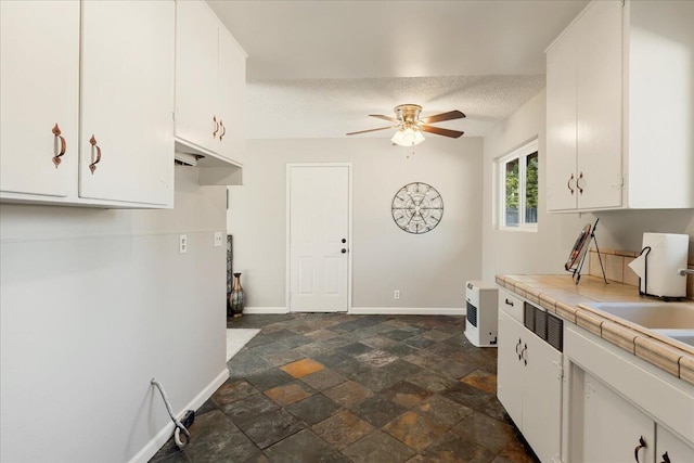 kitchen featuring a textured ceiling, tile counters, and white cabinets