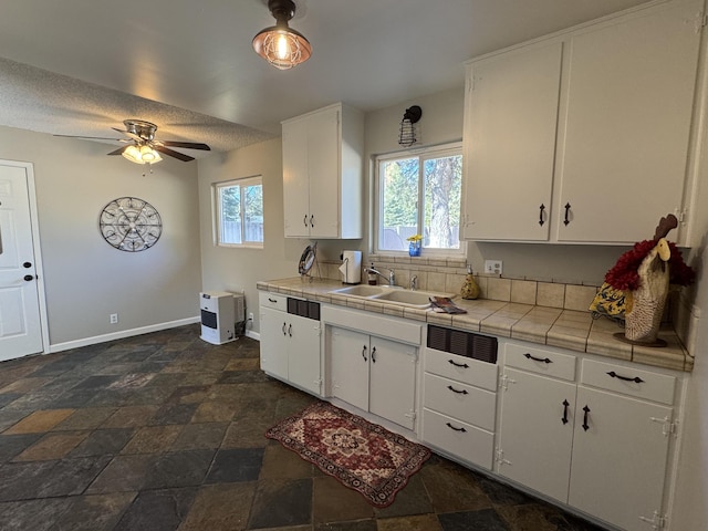 kitchen featuring ceiling fan, tile countertops, sink, and white cabinets