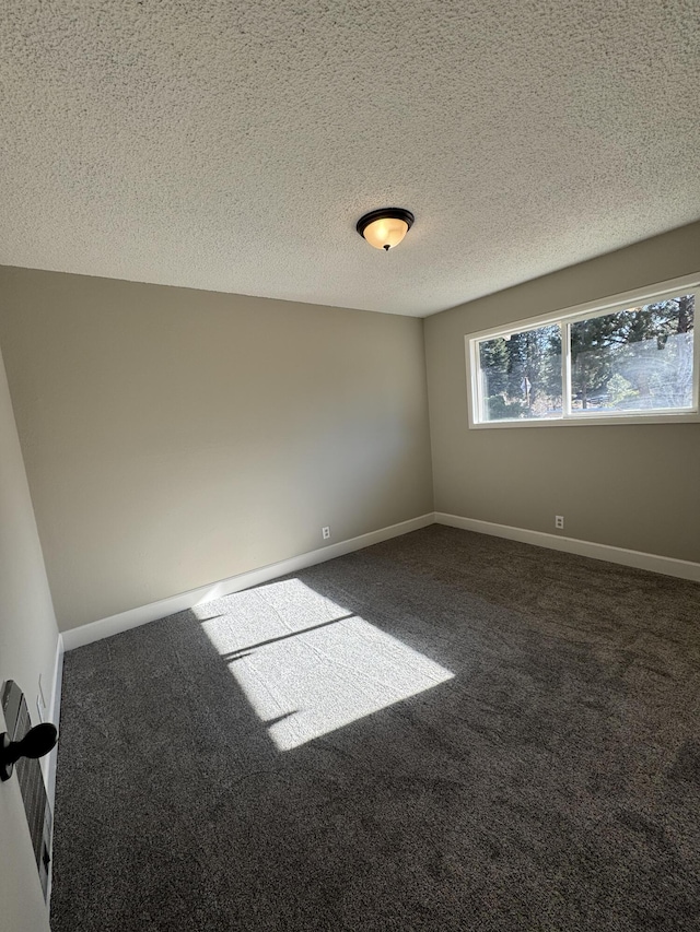 spare room featuring a textured ceiling and dark carpet