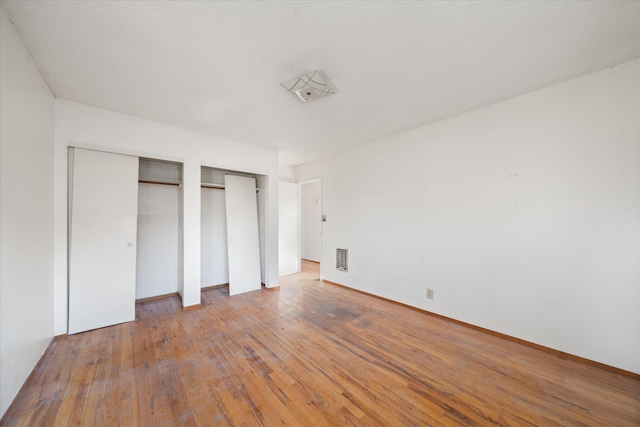 unfurnished bedroom featuring hardwood / wood-style flooring and multiple closets