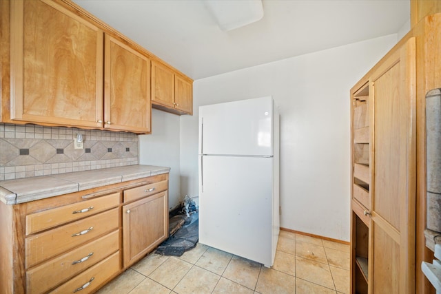 kitchen with tile counters, light tile patterned floors, white fridge, and backsplash