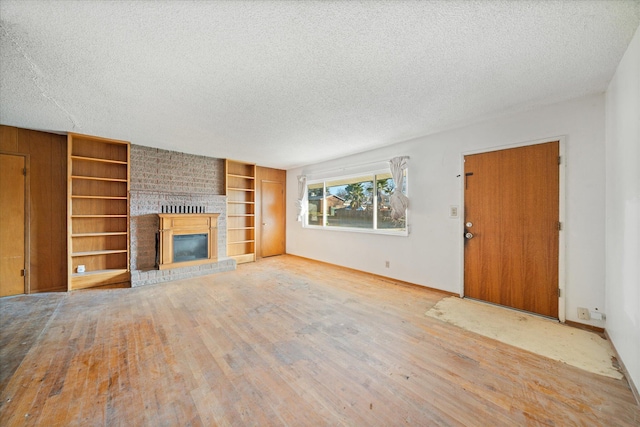 unfurnished living room with a textured ceiling, a fireplace, built in features, and wood-type flooring