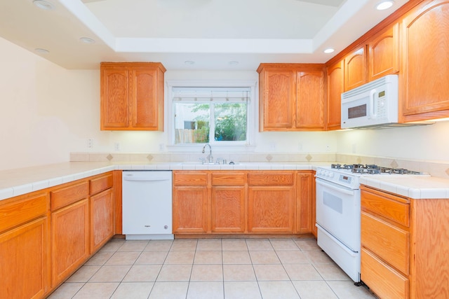 kitchen with light tile patterned flooring, sink, tile counters, a raised ceiling, and white appliances