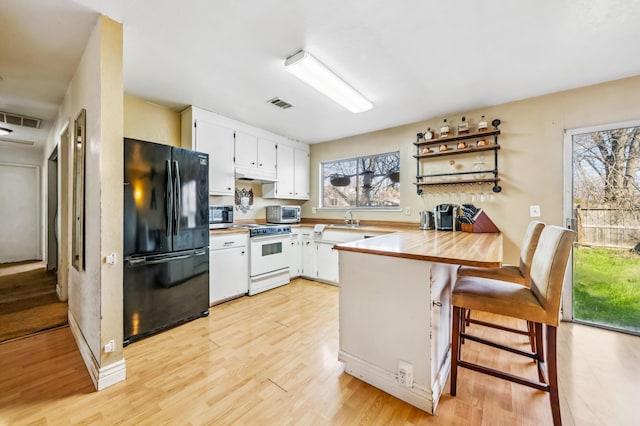 kitchen featuring white cabinetry, black refrigerator, a kitchen breakfast bar, kitchen peninsula, and white range with electric stovetop