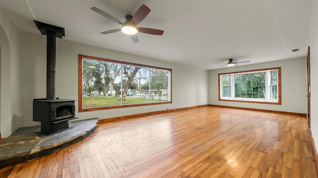 unfurnished living room featuring wood-type flooring, a wood stove, and ceiling fan