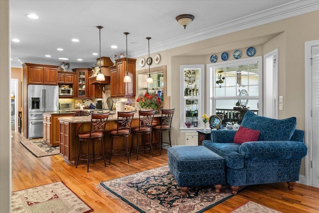 kitchen featuring pendant lighting, a kitchen breakfast bar, light stone counters, stainless steel appliances, and crown molding