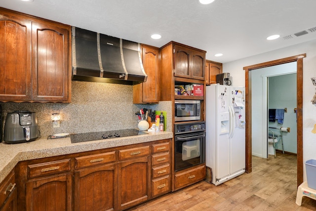 kitchen with light hardwood / wood-style flooring, wall chimney range hood, backsplash, and black appliances